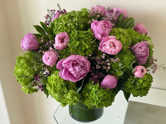 Low round arrangement of bright green hydrangeas and pink peonies in a clear glass cylinder vase.
