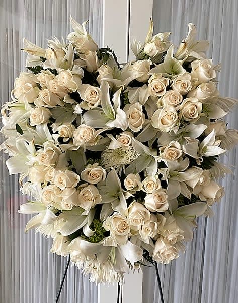 Heart-shaped standing spray of ivory roses and white lilies on a metal easel
