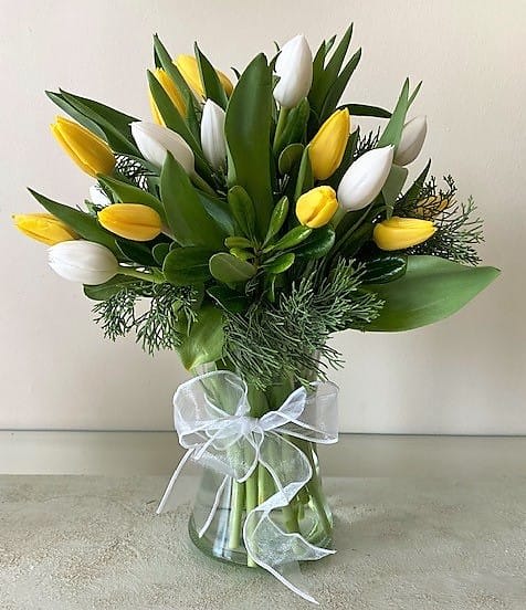Yellow and white tulips arranged in a clear glass vase with a white ribbon bow