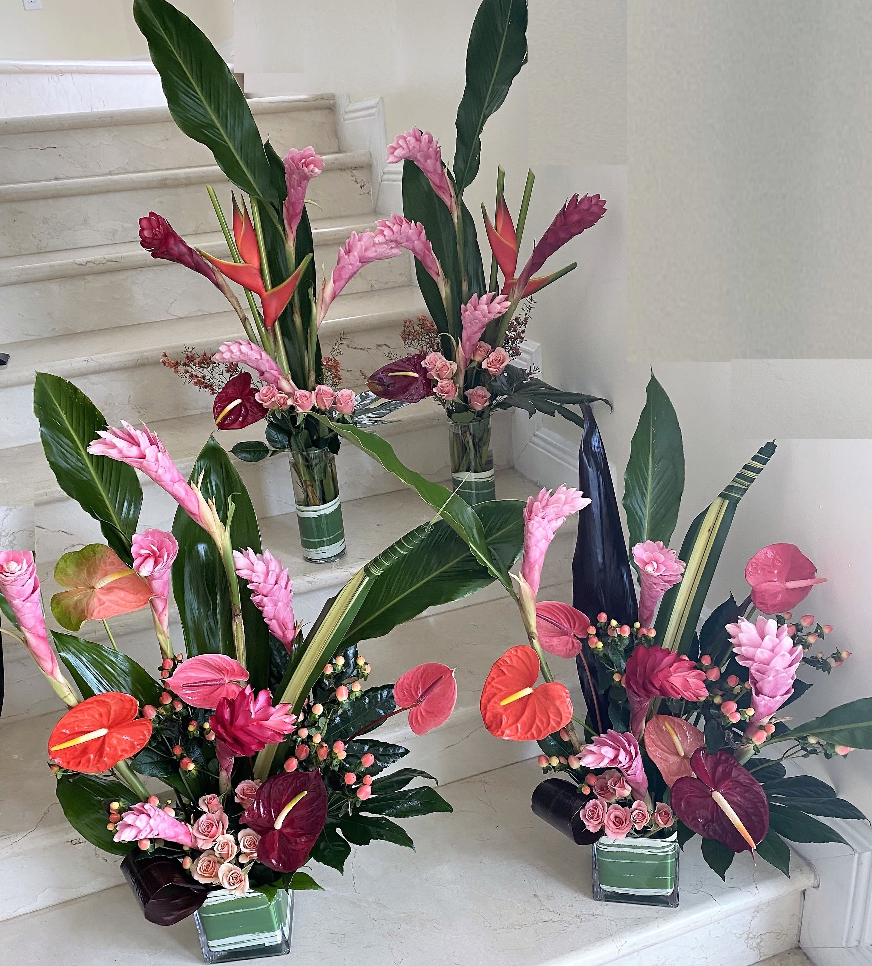 Set of three tall tropical arrangements with pink gingers, anthuriums, and roses in glass vases