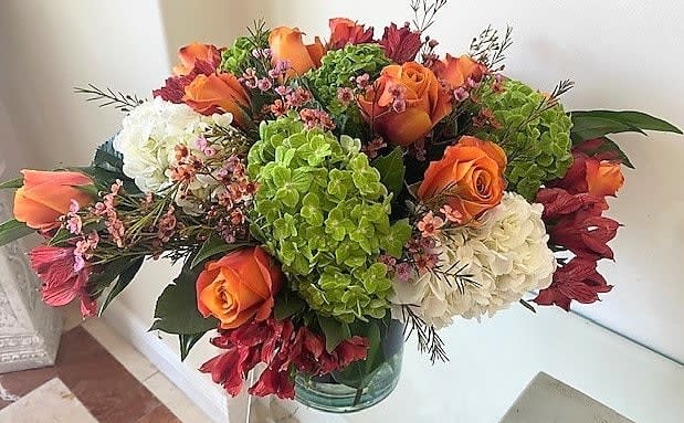 Low glass vase of orange roses, green and white hydrangeas, and red accent flowers.