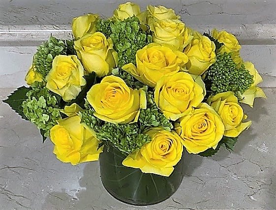 Low arrangement of yellow roses with green accents in a clear glass cylinder vase