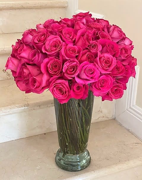 Tall clear glass vase filled with many hot pink roses on a stone step