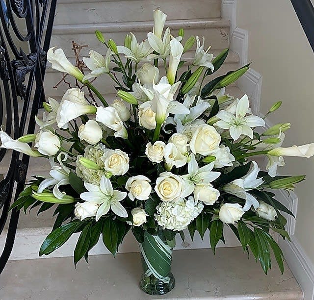 Tall white arrangement of roses, lilies, and calla lilies in a clear glass vase