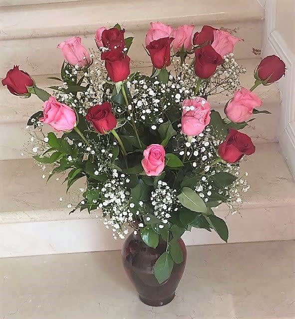 Tall arrangement of red and pink roses with white filler flowers in a dark vase