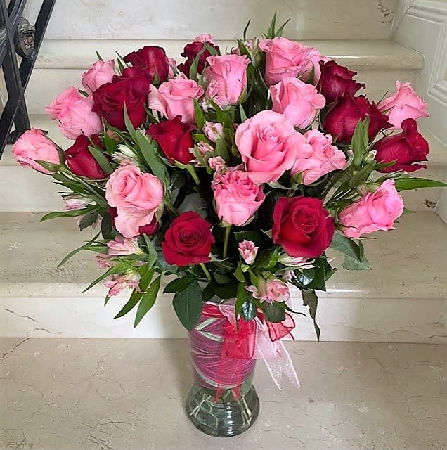 Tall vase of pink and red roses with pink filler flowers and ribbon on a marble step