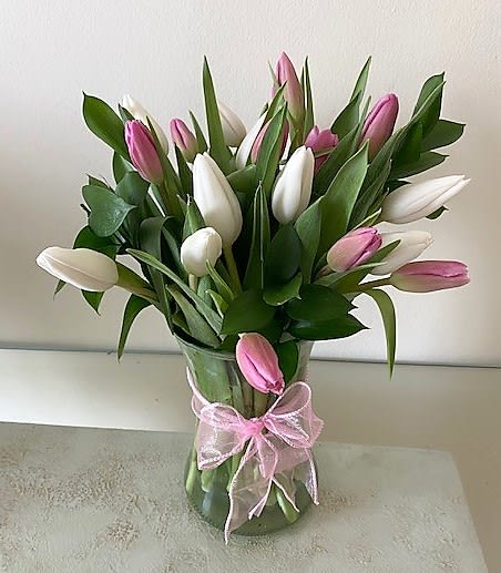 Pink and white tulips arranged in a clear glass vase tied with a pink ribbon bow