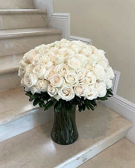 Large arrangement of white and cream roses in a clear glass vase on marble steps