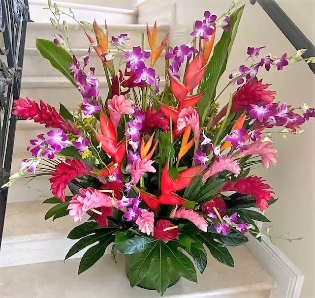 Tall tropical arrangement with pink gingers, orange heliconias, and purple orchids in a green pot