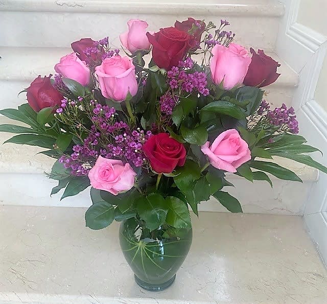Arrangement of pink and red roses with small purple flowers in a green glass vase