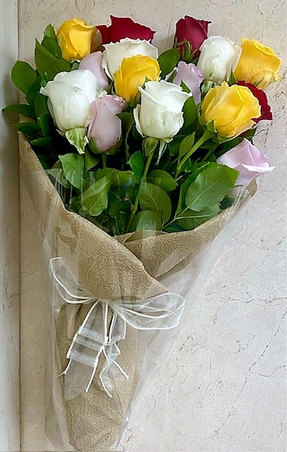 Wrapped bouquet of red, white, yellow, and pink roses in patterned paper with a white ribbon