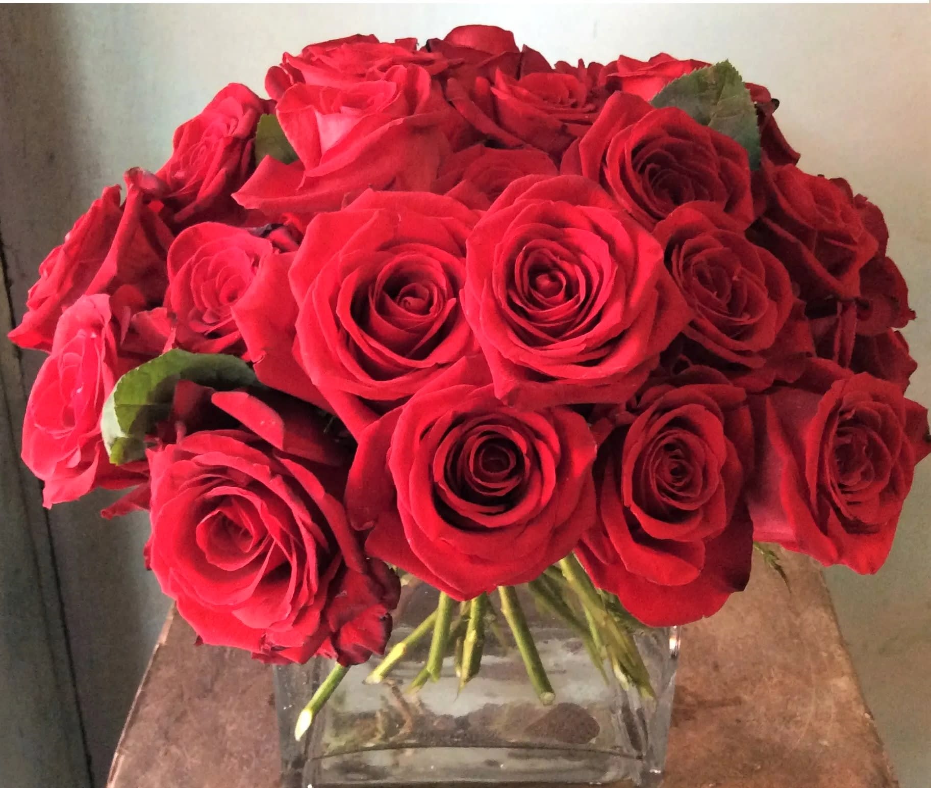 Tight cluster of red roses arranged in a clear square glass vase