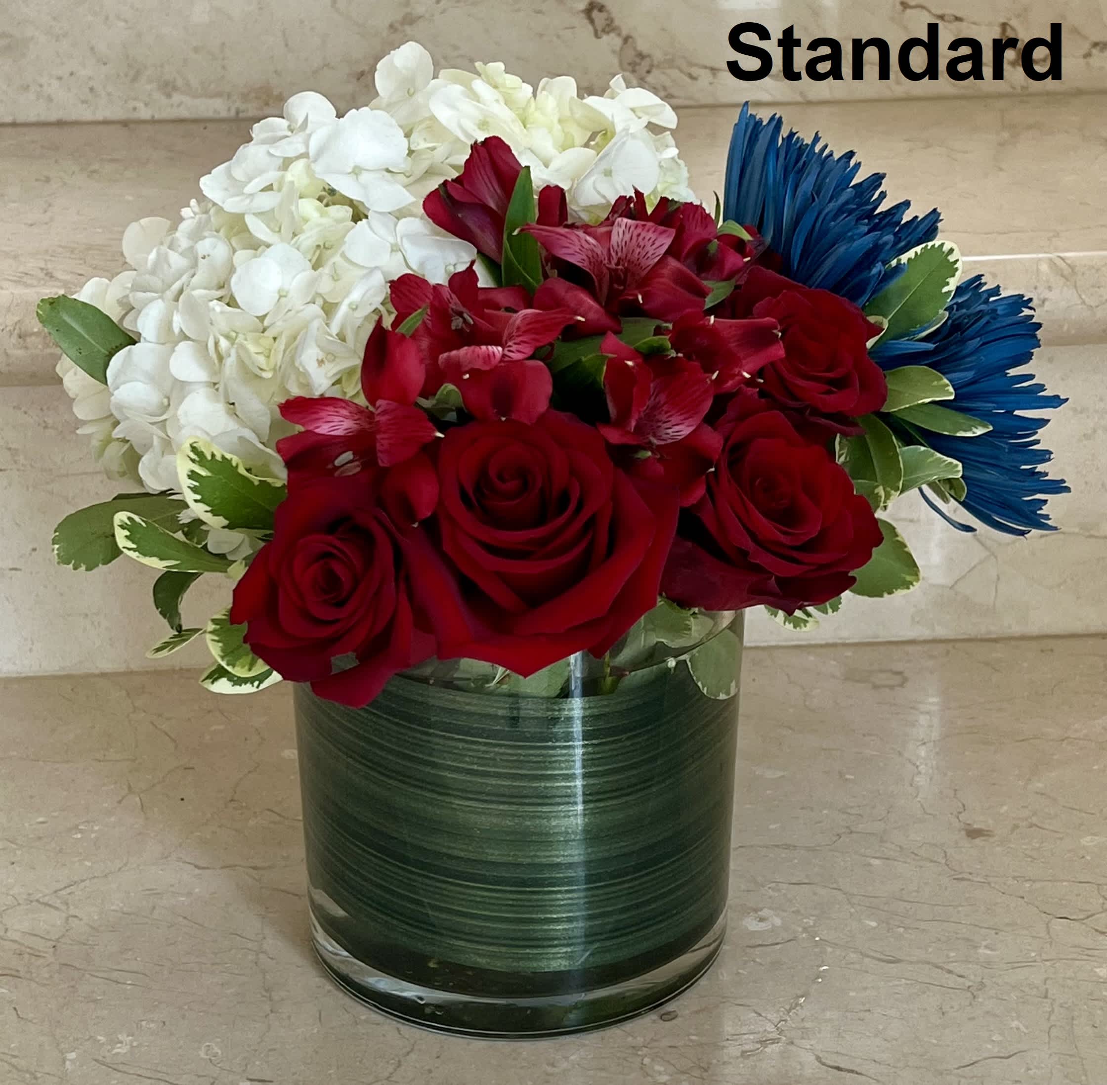 Red roses, white hydrangeas, and blue daisies in a glass vase