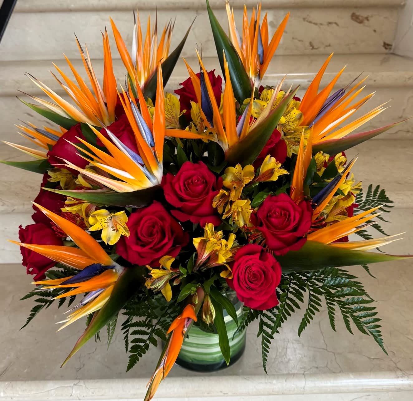 Bouquet of red roses and orange bird of paradise in a glass vase