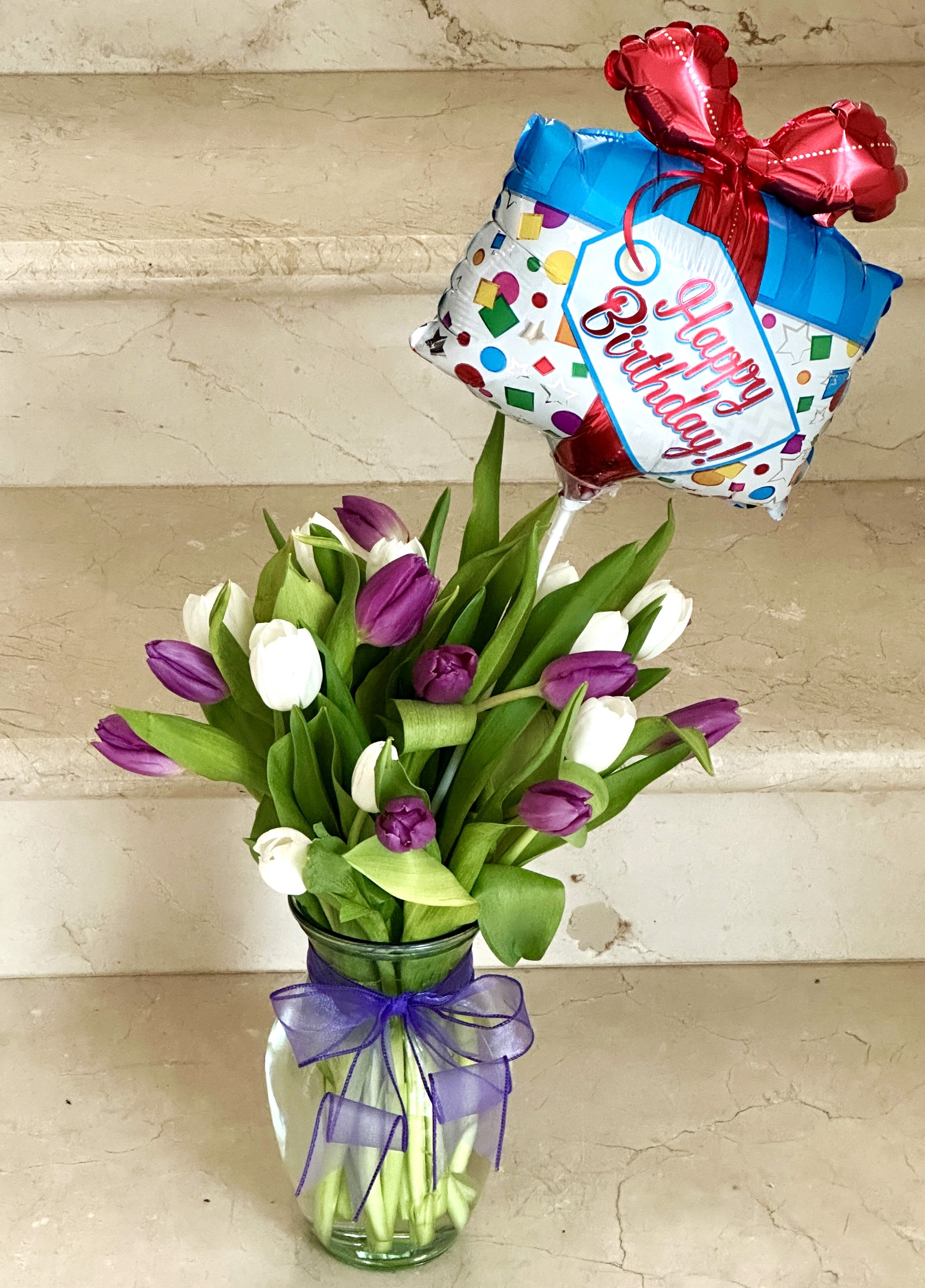 Purple and white tulips in a glass vase with a birthday balloon