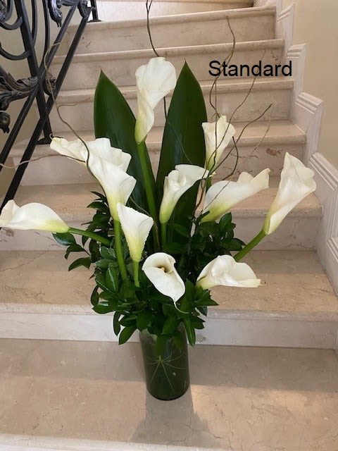 Tall arrangement of white calla lilies in a clear glass vase on stone steps