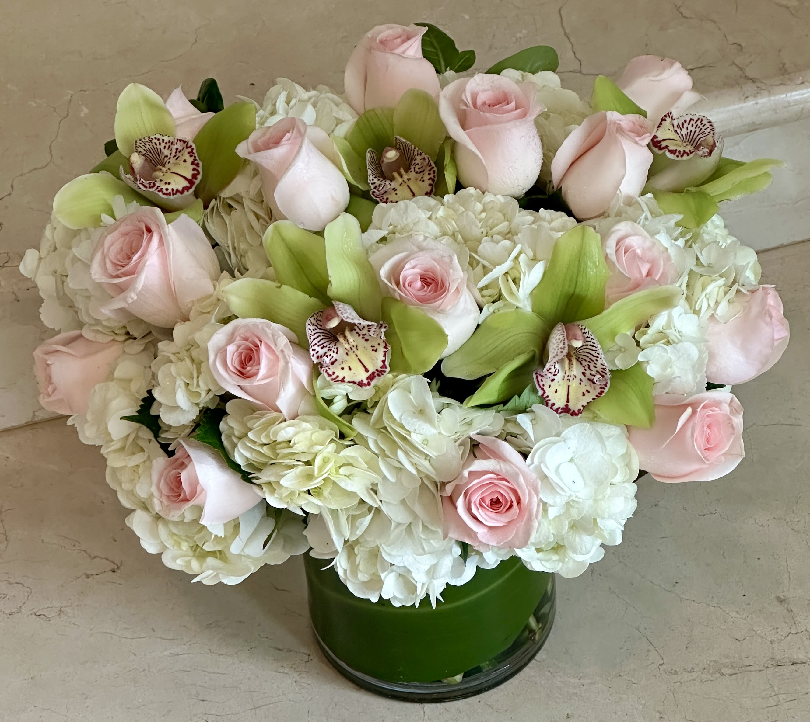 Pink roses and white hydrangeas with green orchids in a glass vase