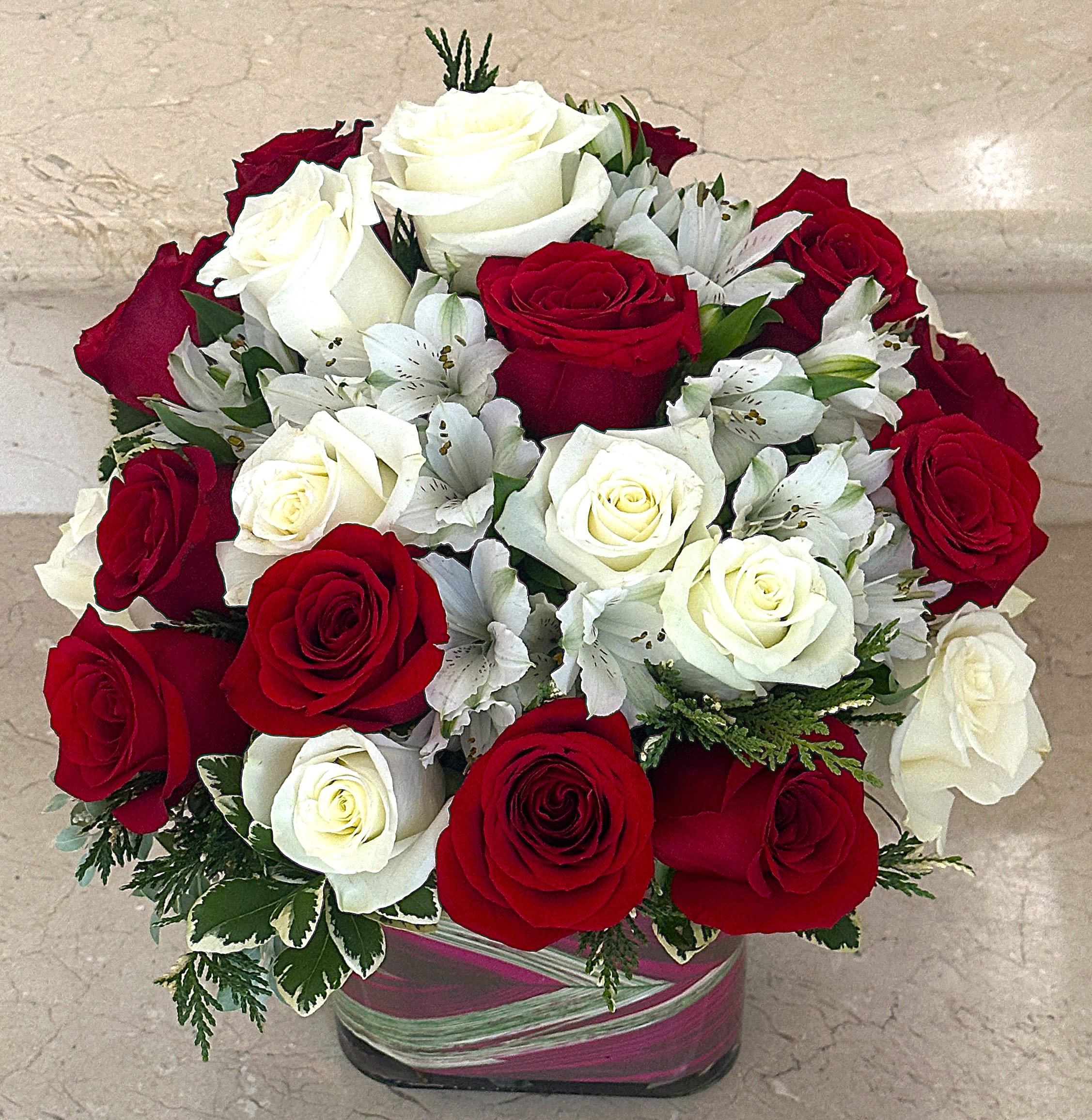Compact arrangement of red and white roses with white alstroemeria in a ribbon-wrapped glass cube vase
