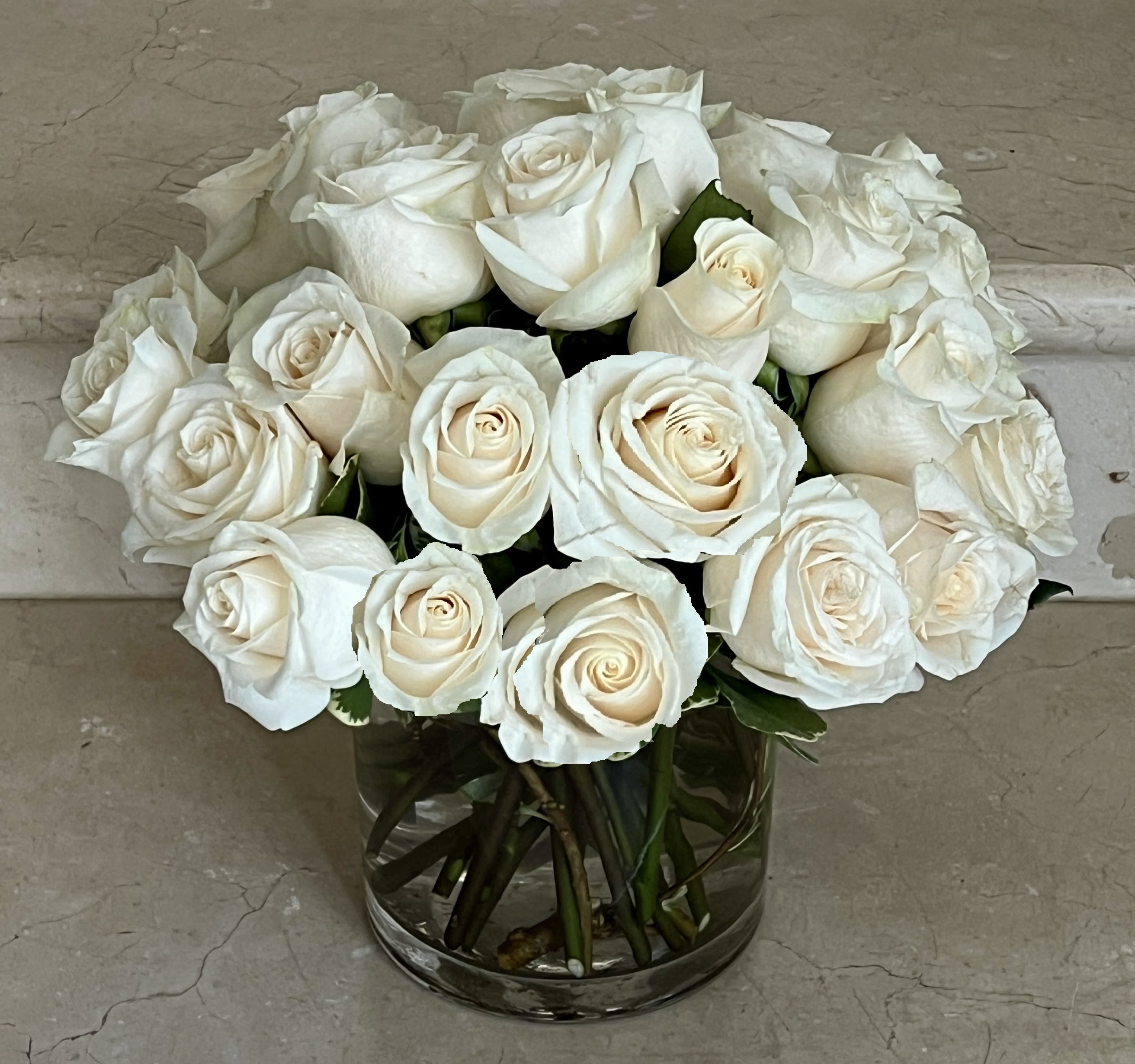 Compact arrangement of ivory white roses in a clear glass cylinder vase