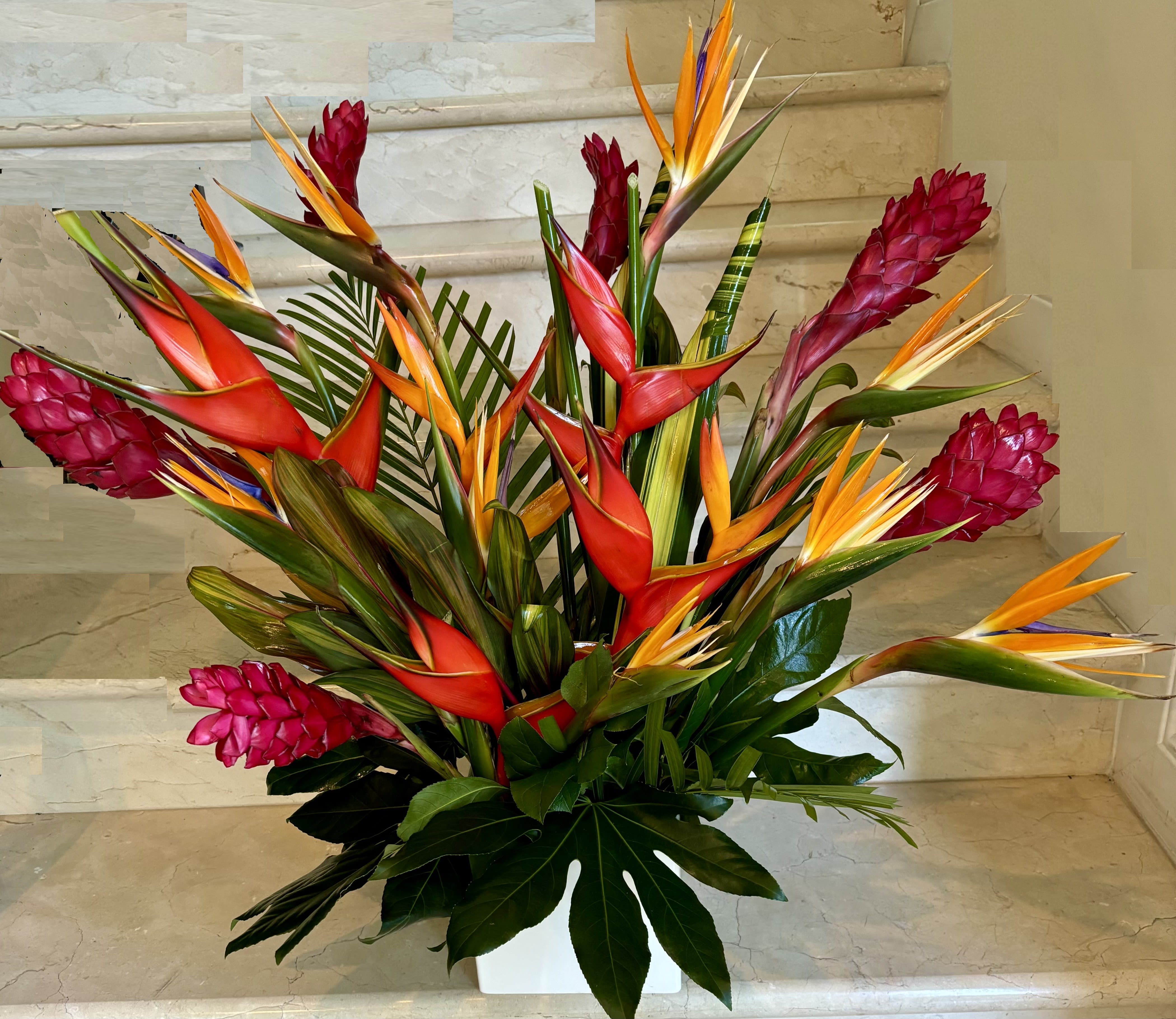 Tropical arrangement with red and orange bird-of-paradise flowers in a white vase