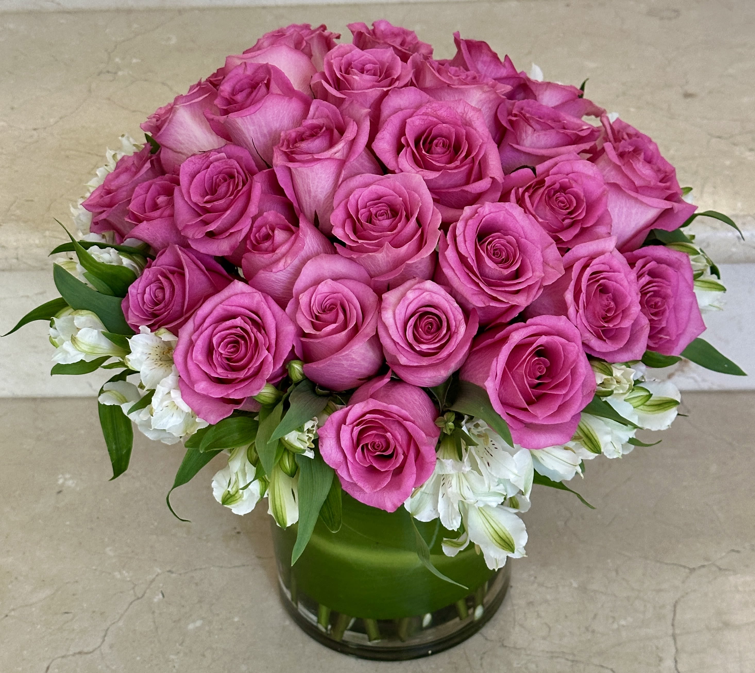 Pink roses arranged in a clear glass vase with white flowers around the base