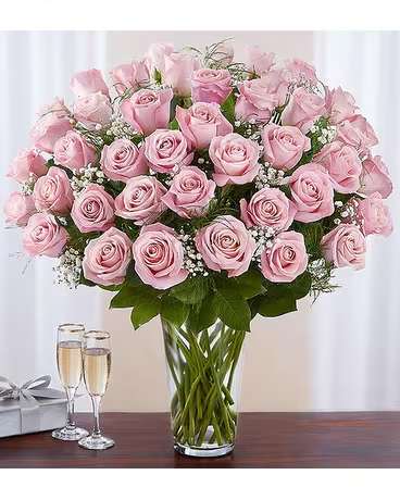 Pink roses arranged in a clear glass vase with a gift box and champagne flutes nearby