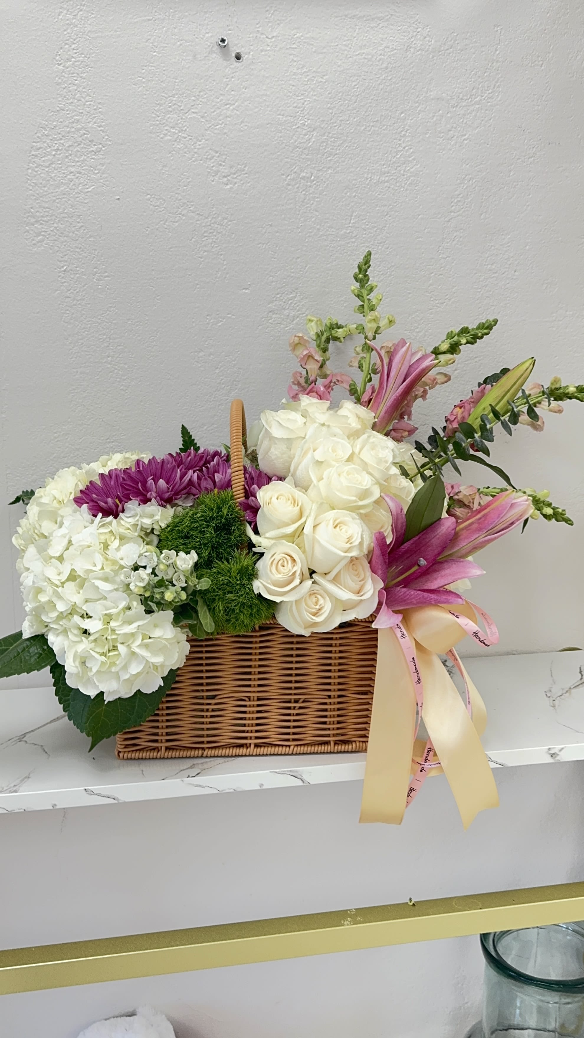 Basket arrangement of white roses, hydrangeas, and pink lilies with ribbon