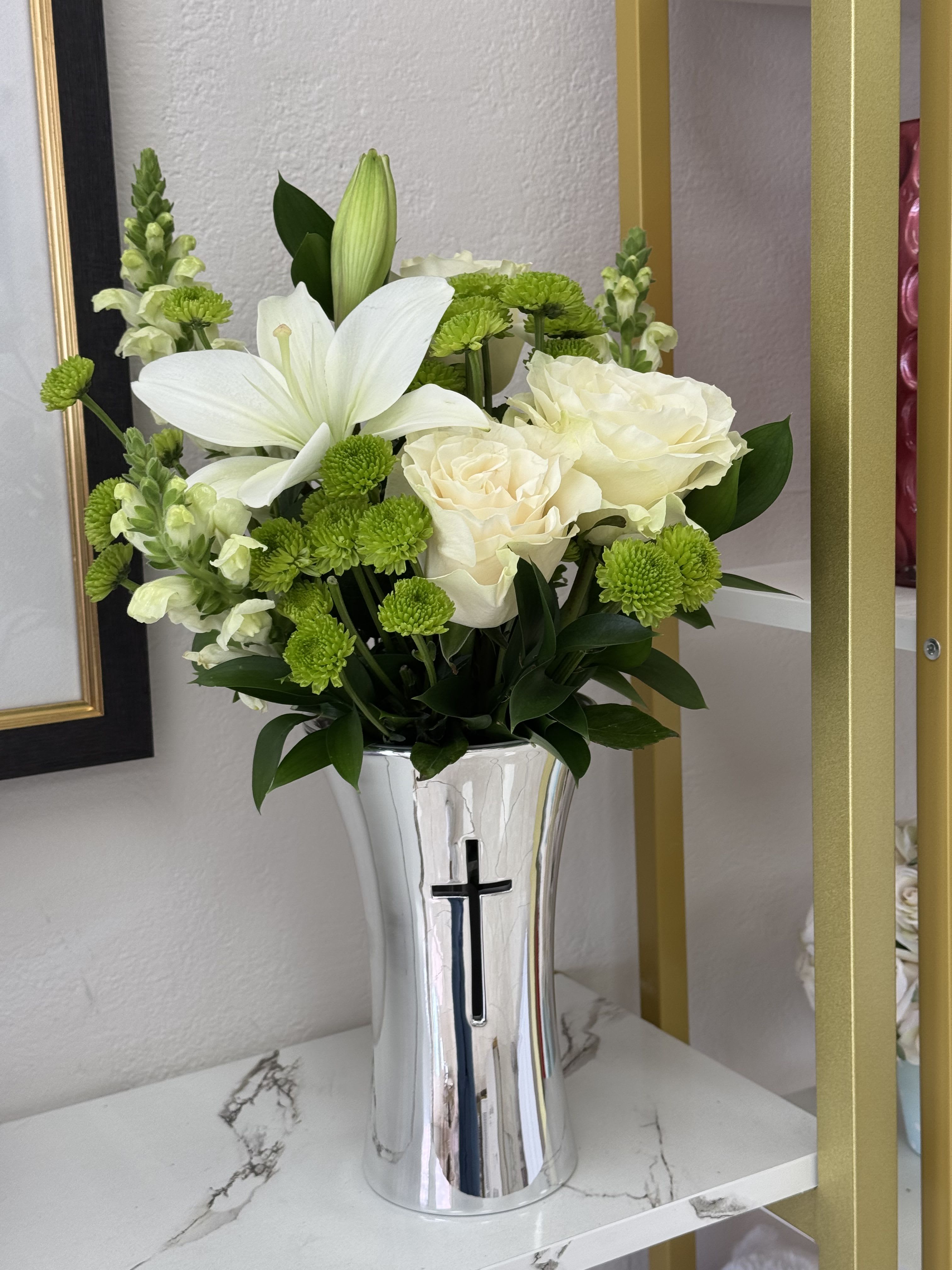 White lilies and roses in a silver vase with a cross
