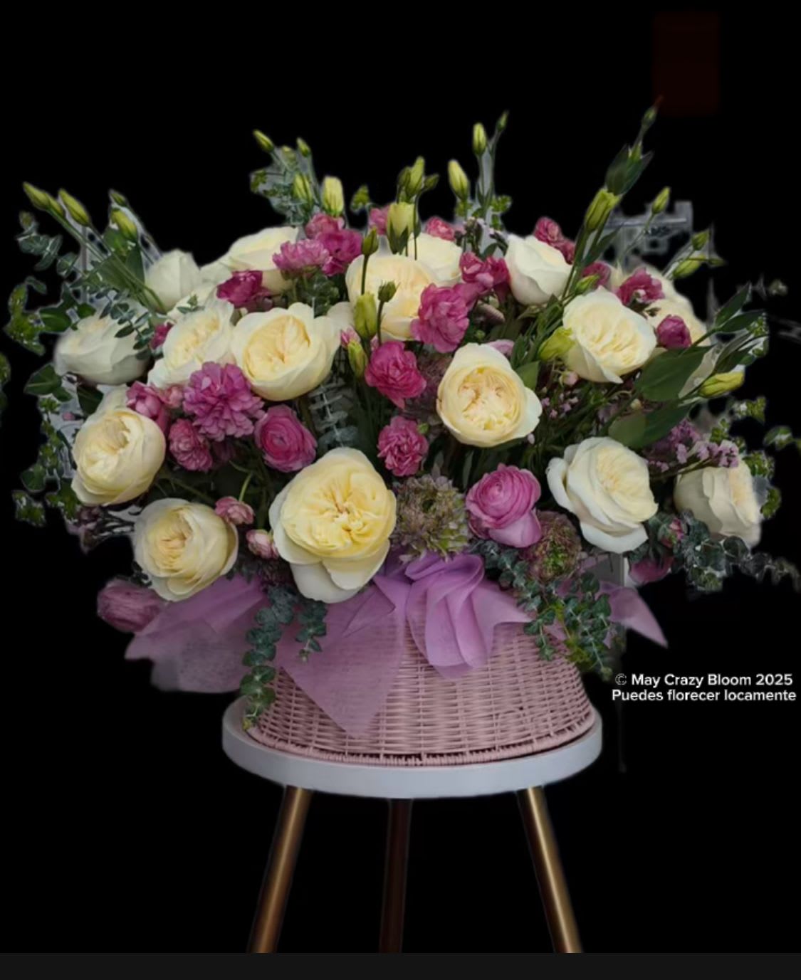 Pink and cream roses arranged in a wicker basket with a lavender ribbon.