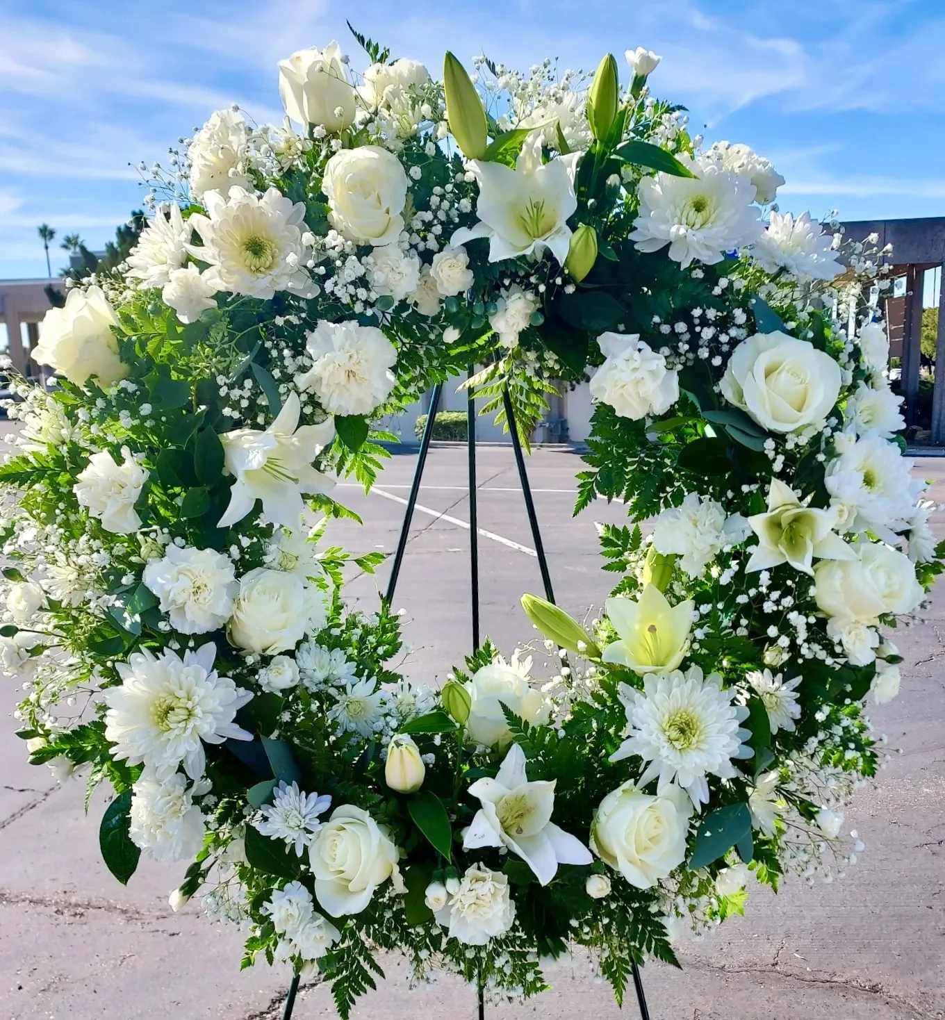 White floral wreath on a black stand outdoors