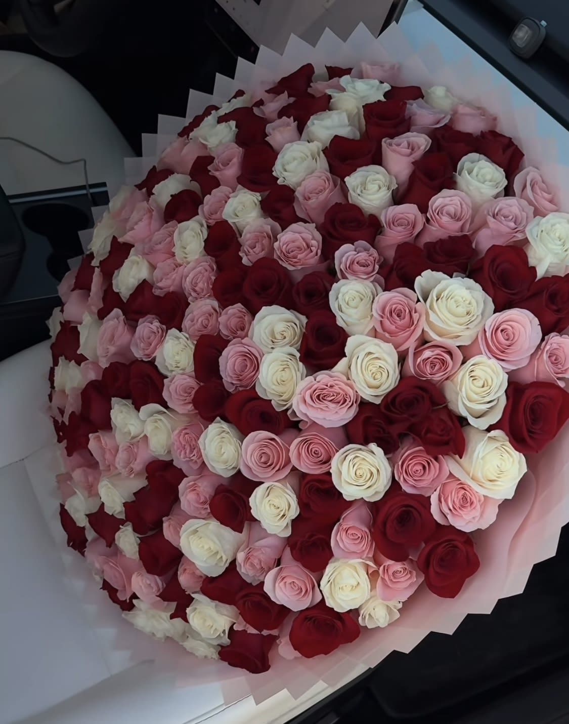 Large bouquet of red, pink, and white roses wrapped in pale pink paper