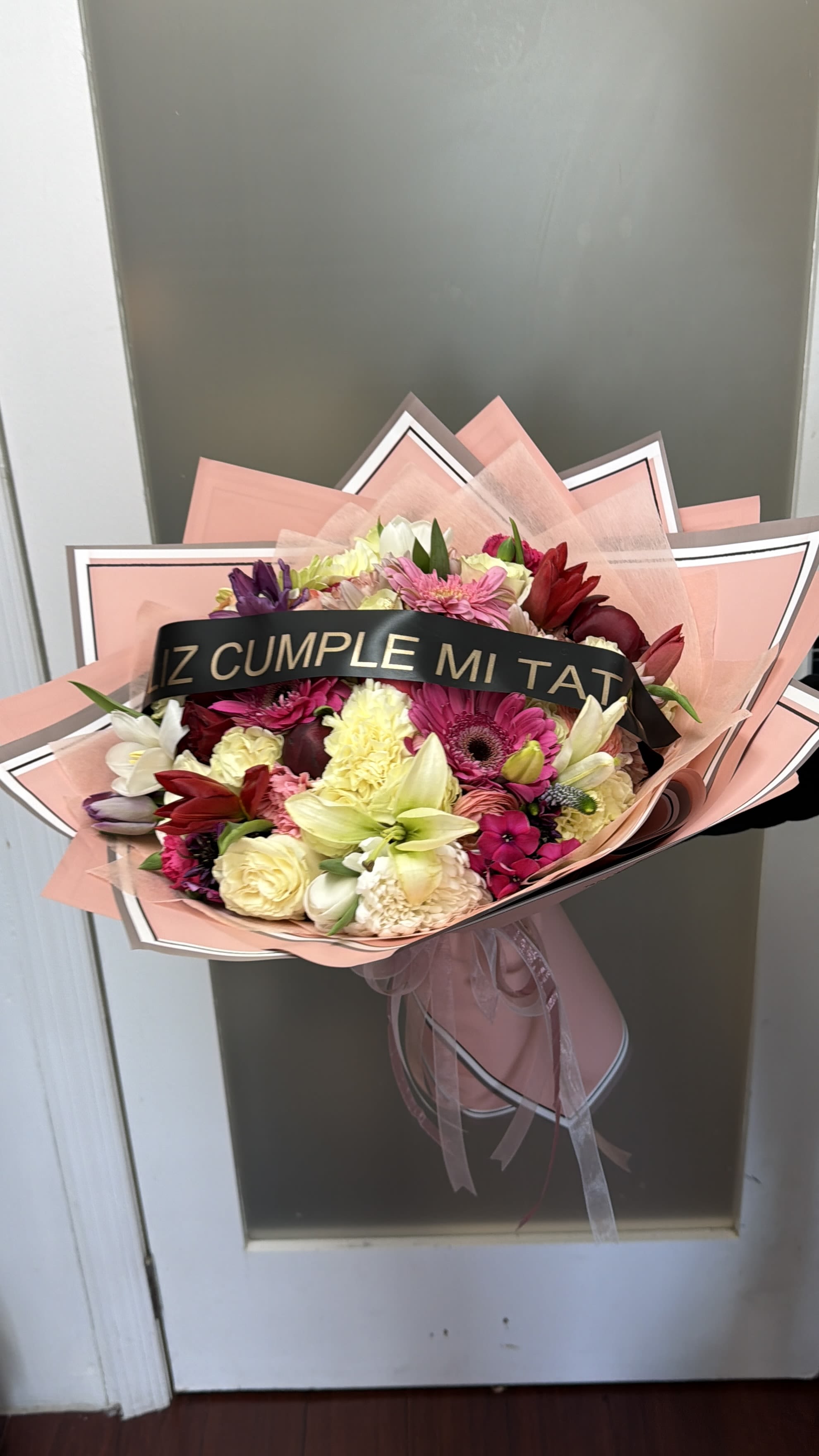Mixed bouquet of pink, red, white, and yellow flowers wrapped in pink paper