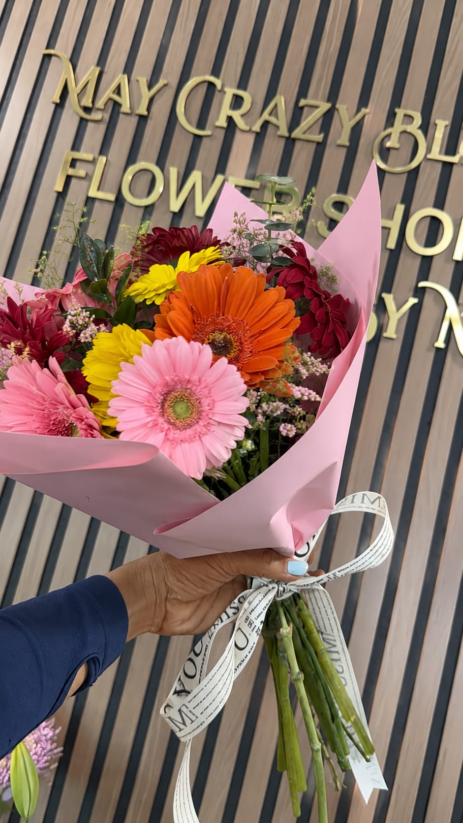 Gerberas  - A lively burst of color made to make someone smile - this gerbera bouquet is a bright everyday arrangement perfect for birthdays, thank-you gestures, or a just-because surprise. The arrangement's cheerful mix of gerbera daisies and chrysanthemums in pink, light pink, orange, yellow and deep red reads playful and celebratory, so the person you're sending it to will feel noticed and uplifted the moment it arrives.  Tightly gathered (or for the looser option, hand-tied) blooms are wrapped in soft pink paper and finished with a printed ribbon for a fresh, gift-ready presentation that looks handmade. Large gerbera heads provide bold focal color while chrysanthemums add texture and fullness; the overall palette reads warm and energetic. Ideal for coworkers, friends, and family who appreciate bright, happy flowers - note that this design arrives wrapped in pink paper with a printed ribbon and is best enjoyed kept in fresh water with stems recut every few days.