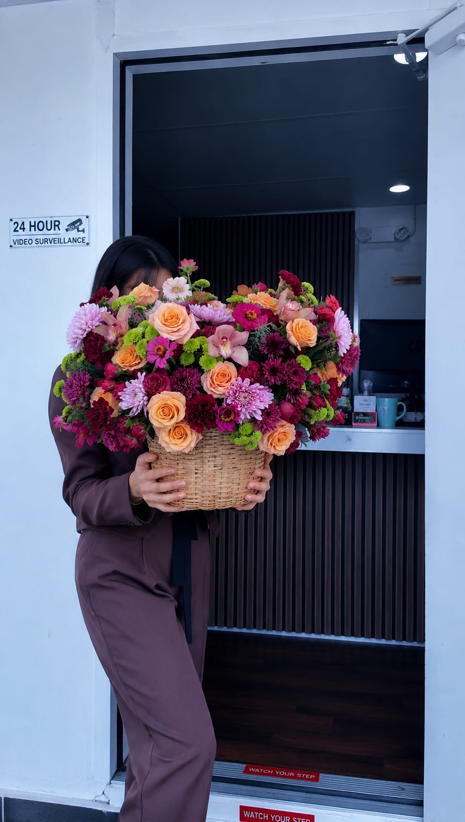 I dit it May Way - A lush, overflowing basket arrangement that feels like a joyful celebration in bloom - perfect as a birthday bouquet, anniversary surprise, or a generous thank-you gift. This flower arrangement for gifting mixes peach roses and saturated pink chrysanthemums with deeper burgundy mums and a few delicate orchid-like blooms to create a romantic, cheerful display your recipient will remember.  Densely packed into a rounded, abundant shape, the flowers sit in a handwoven basket that gives the piece a rustic, hand-delivered warmth. Bright green accent blooms weave through the peach, pink, and purple palette for lively contrast and visual depth; the result reads both elegant and exuberant. The full scale of the design makes it a standout centerpiece or a heartening room brightener.  Send this to make someone feel genuinely celebrated - whether marking a milestone, saying thanks, or simply bringing everyday joy. The woven basket arrives ready to display; light trimming of stems and fresh water will keep the blossoms looking their best during the first week.