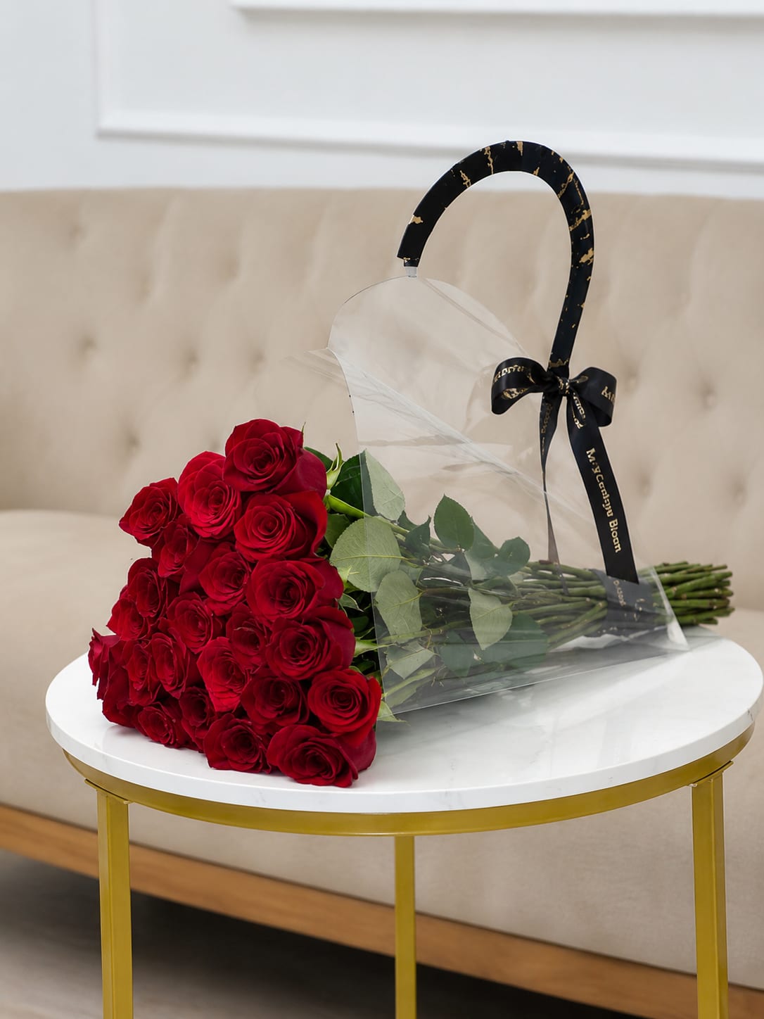 On Point - A dense cascade of deep red roses tied with a sleek black ribbon gives this flower arrangement a boldly romantic, polished look perfect for anniversary roses, Valentine's Day, or a striking Father's Day gift. The tight clusters of velvety red blooms read as classic and confident-she or he will feel truly seen when presented with this elegant bouquet for birthdays, graduations, retirements, or simply to say "thinking of you."  Each long-stemmed rose is gathered with fresh green foliage and wrapped in clear plastic that keeps the arrangement crisp and ready to display. The transparent sleeve showcases the rich color while the black ribbon adds modern contrast, making it equally at home for holiday table accents (Thanksgiving, Christmas), autumn and winter celebrations, or a sophisticated housewarming or wedding touch. Size and stem count are those of a generous, gift-ready bouquet; stems arrive wrapped for protection and should be recut and placed in fresh water to extend vase life.