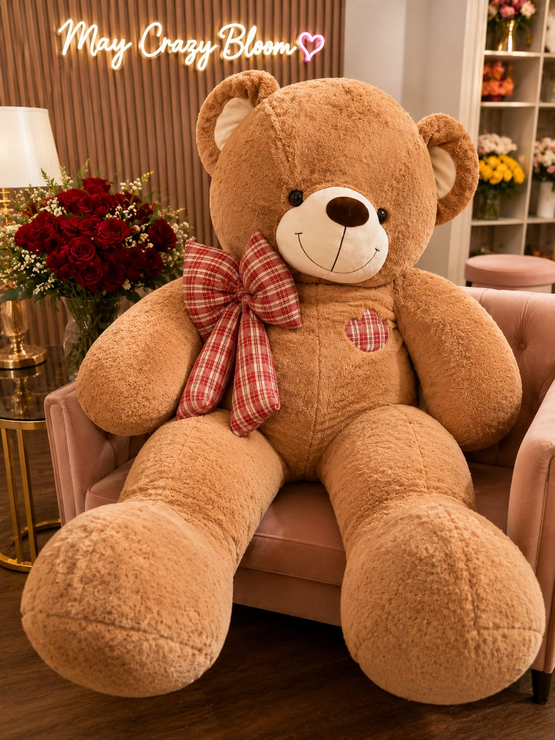 Large teddy bear with a plaid bow sitting beside a bouquet of red roses