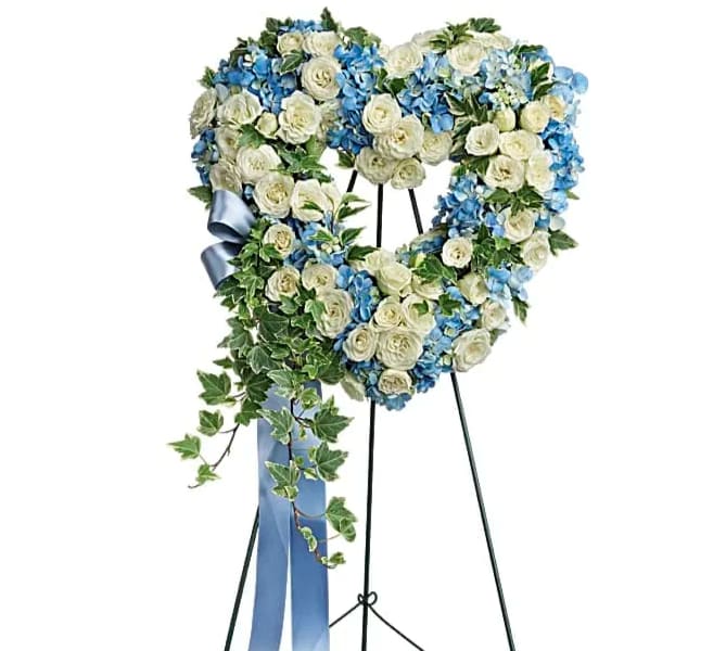 Heart-shaped floral wreath of white roses and blue flowers on a stand