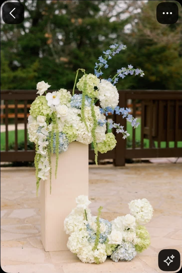 Wedding floral arrangement with white, pale green, and light blue flowers on a pedestal