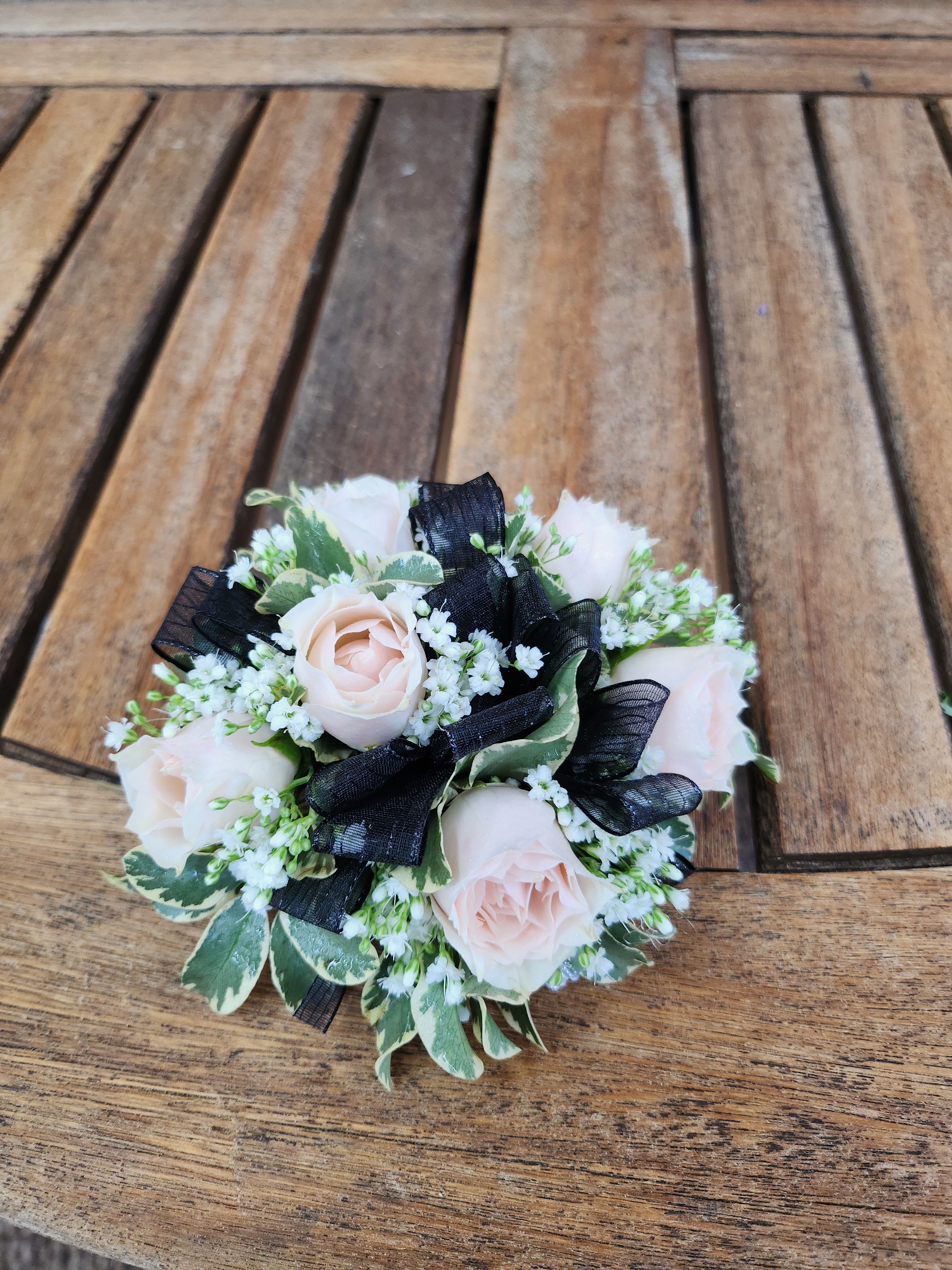 Small bouquet of pale pink roses with black ribbon on a wooden surface