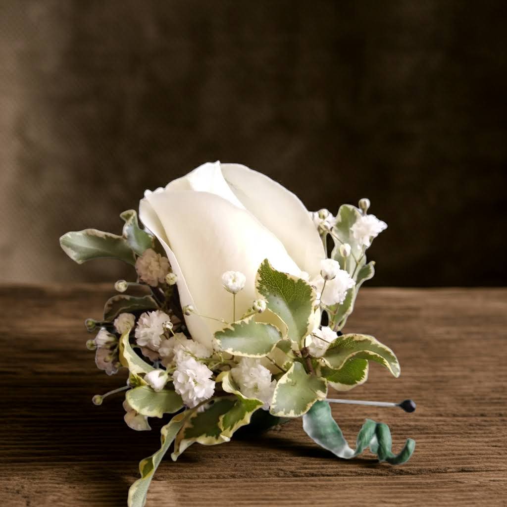 White rose boutonniere with small white filler flowers and variegated greenery