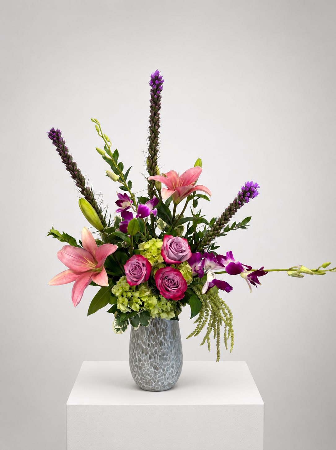 Pink lilies and roses in a gray vase with purple orchids