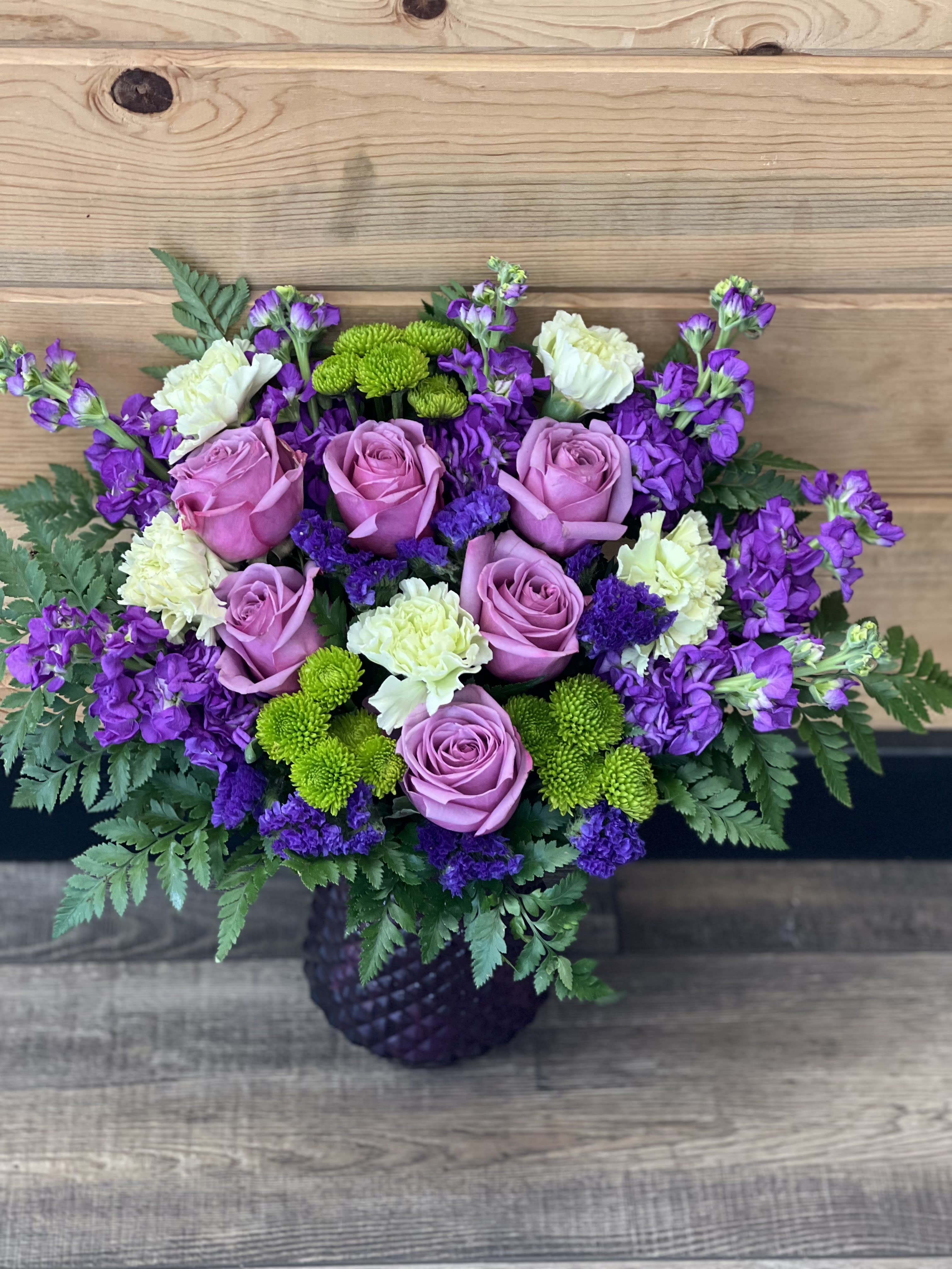 Bouquet of pink roses, purple flowers, and green mums in a dark vase