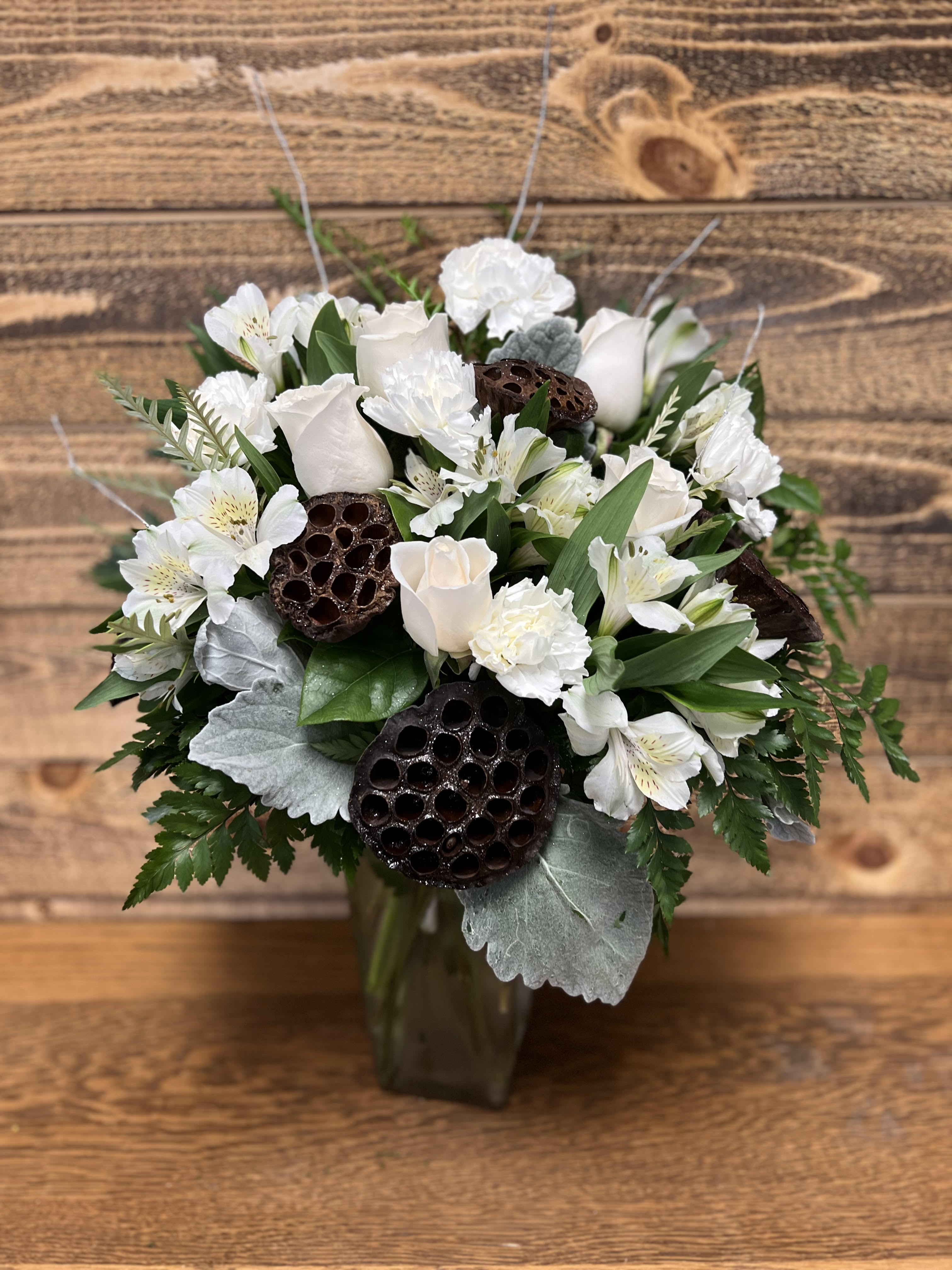 White floral arrangement in a glass vase with lotus pods and silver foliage