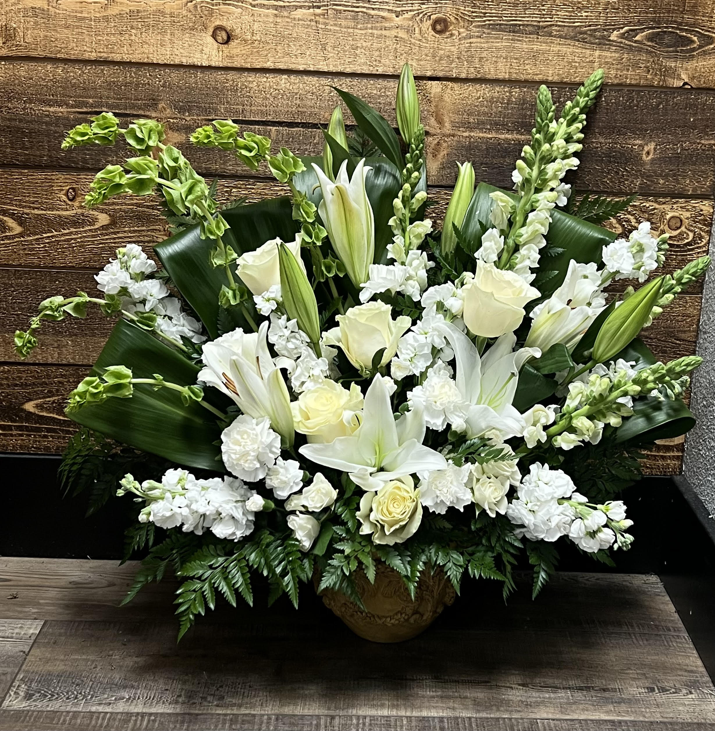 White lilies and roses arranged in a low urn with greenery