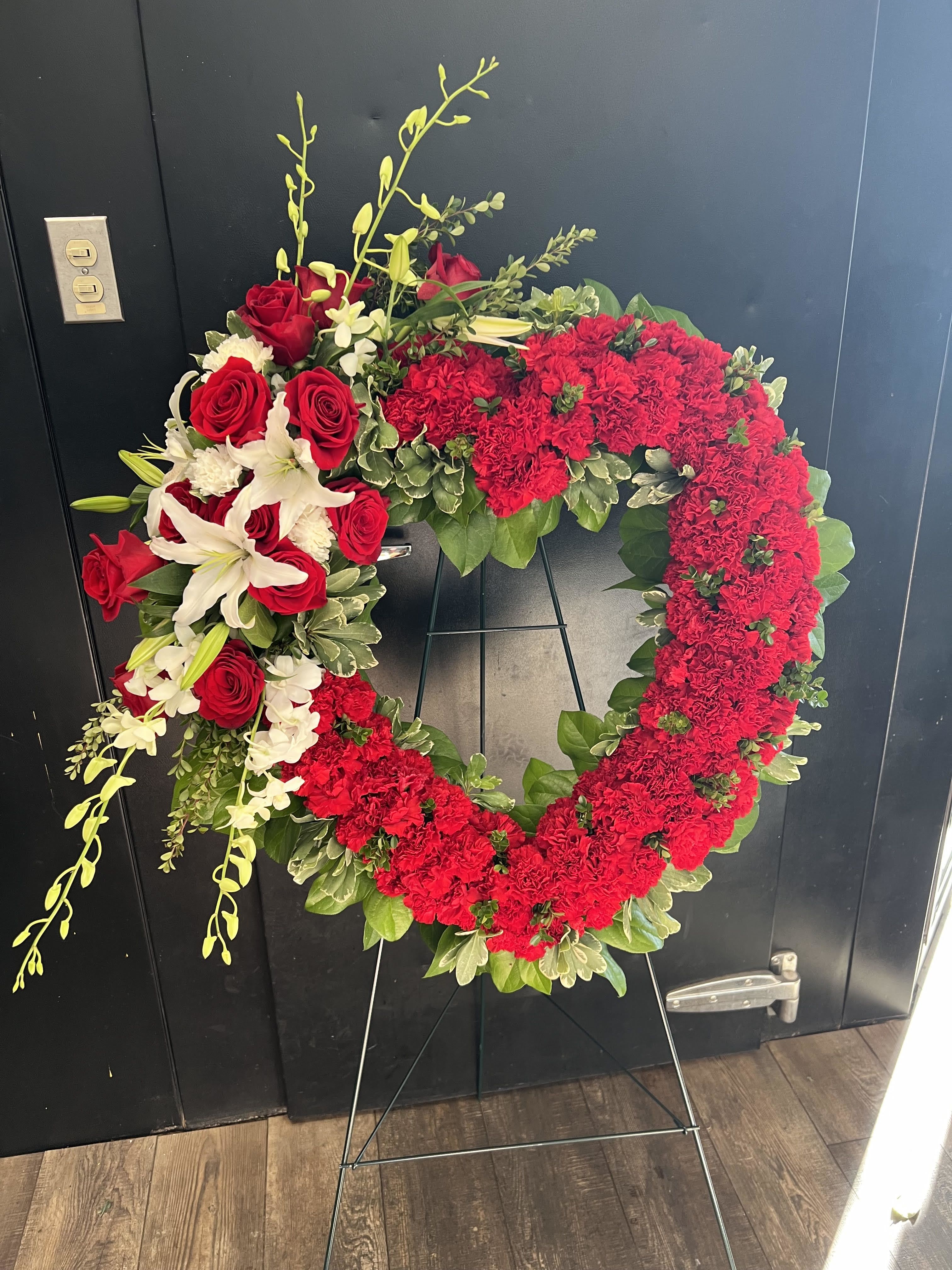 Heart-shaped red floral wreath on a stand with white lilies and roses