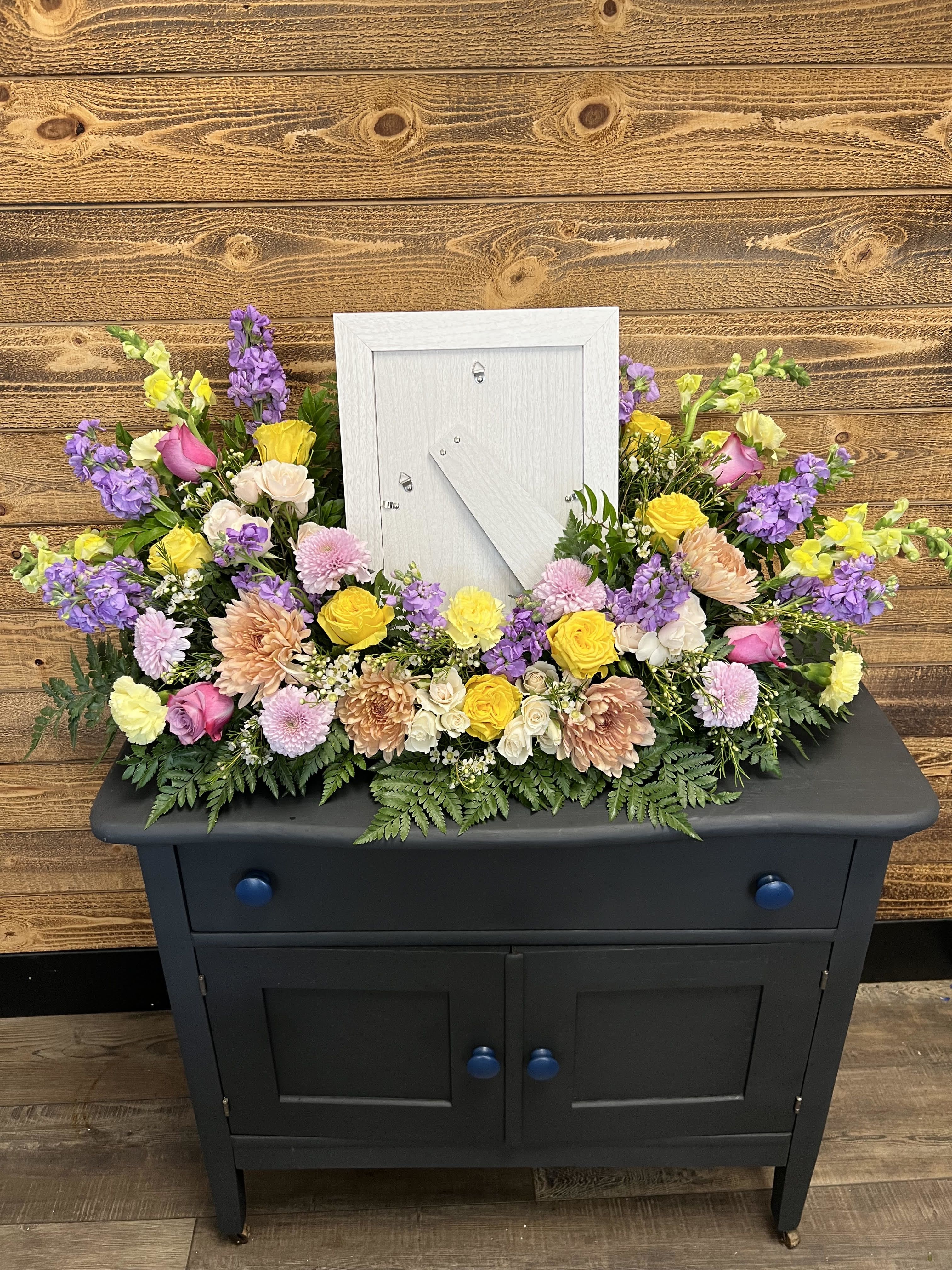 Colorful floral arrangement around a white picture frame on a black cabinet