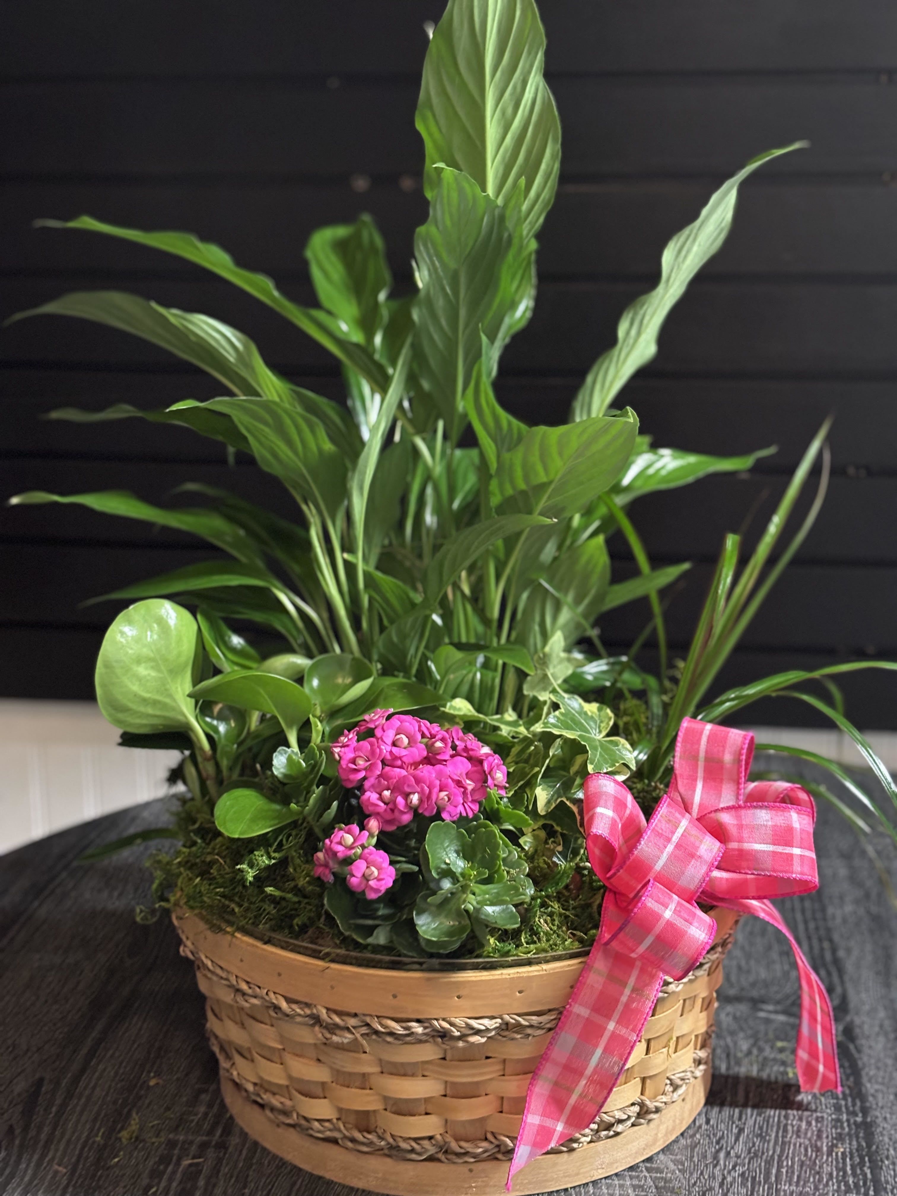Basket planter with pink flowers and assorted green houseplants, tied with a pink ribbon
