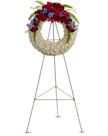 Standing funeral wreath with red roses, white flowers, and blue accents on an easel