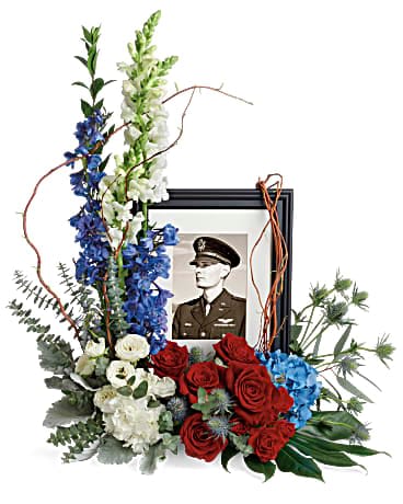 Floral tribute around a framed military portrait with red, white, and blue flowers