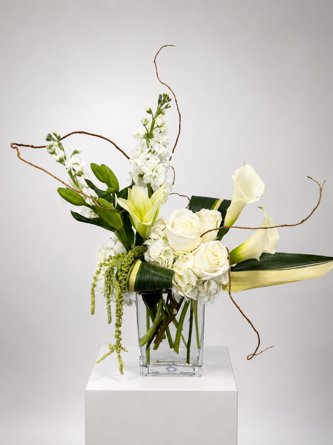 White roses, calla lilies, and orchids in a clear glass vase
